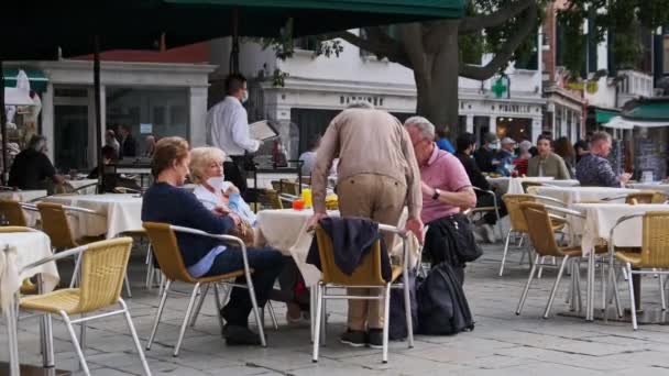 Turisté sedí u stolů restaurací a kaváren na nádvoří Benátek — Stock video