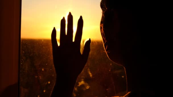 Silhouet vrouw bij het raam putting hand naar glas door zonsondergang stralen Slow motion — Stockvideo