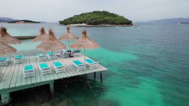 Luftaufnahme leerer Sonnenliegen unter Strohschirmen auf einem Pier im türkisfarbenen Meer — Stockvideo