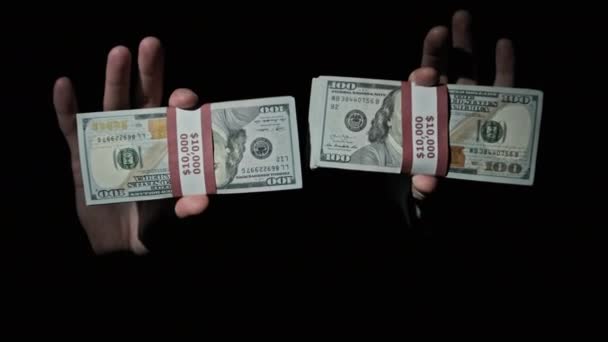 Две пачки по 10000 американских долларов в мужских руках на черном фоне — стоковое видео