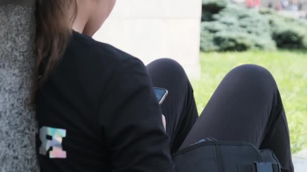 Junge Frau nutzt Smartphone, während sie auf Brüstung im Straßenpark sitzt — Stockvideo