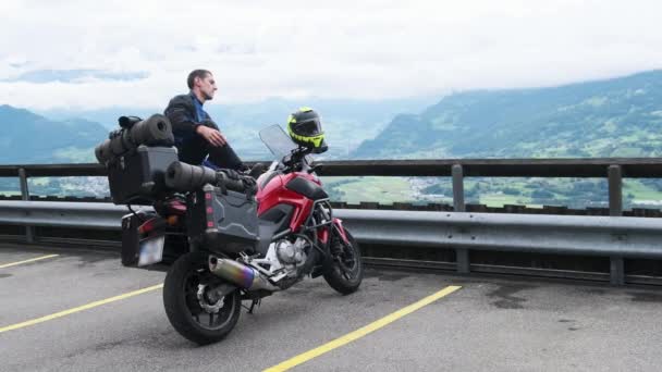 荷物袋付き観光バイクのバイカーは山の風景、アルプスのそばに立つ — ストック動画