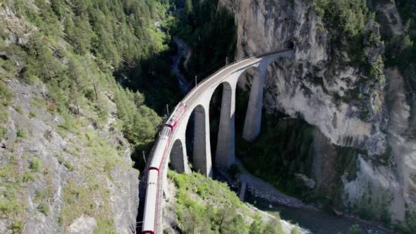 Вид с воздуха на движущийся красный поезд вдоль виадука Landwasser в швейцарских Альпах — стоковое видео