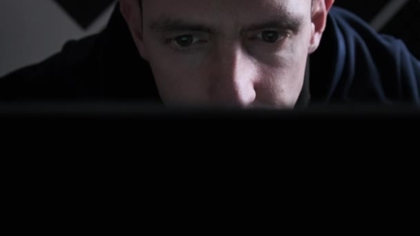Junger Mann blickt zu Hause in einem dunklen Raum auf den Bildschirm eines Laptops — Stockvideo