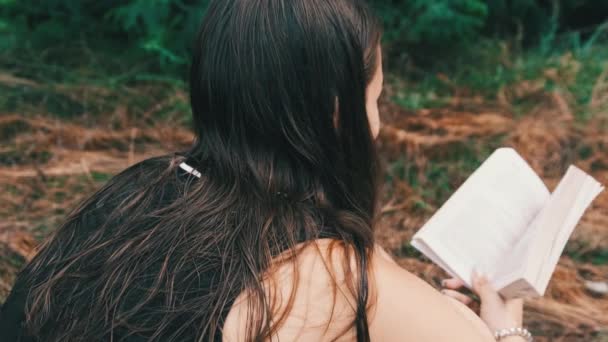 Młoda kobieta czyta książkę siedząc na trawie w przyrodzie w letni dzień — Wideo stockowe