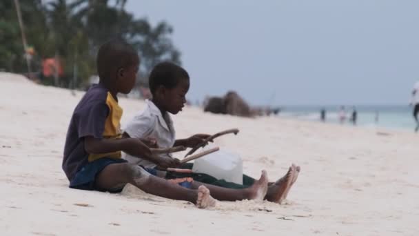 Два местных африканских мальчика сидят на пляже и играют импровизированные бутылочные барабаны, Занзибар — стоковое видео