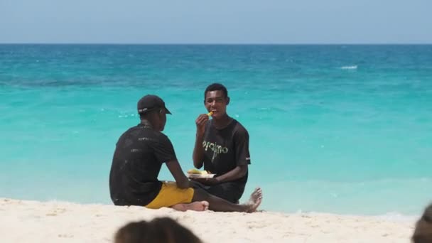 Два африканских подростка едят фрукты на пляже Накупенда в солнечный день, Занзибар — стоковое видео