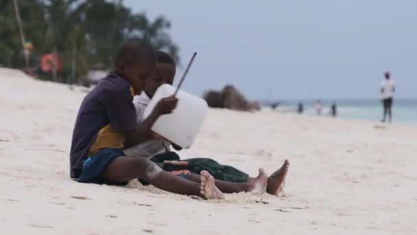 Dois meninos africanos locais sentam-se na praia e tocam tambores de garrafa improvisados, Zanzibar — Vídeo de Stock