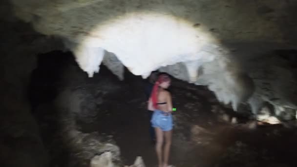 Donna esplora stalattiti all'interno di una profonda grotta oscura, illuminante con torcia elettrica — Video Stock