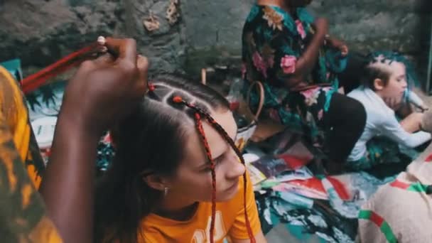 Afrikansk kvinna vävning afrikanska flätor med röd Kanekalon utomhus, Zanzibar Afrika — Stockvideo