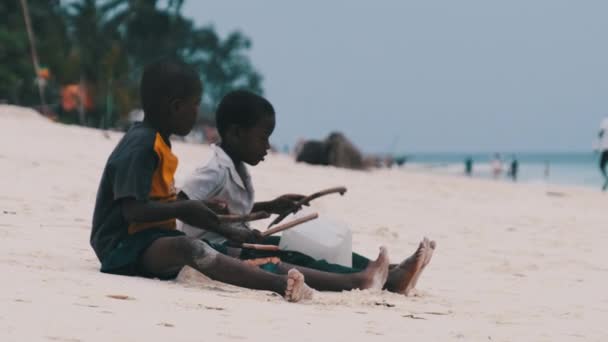 Zwei lokale afrikanische Jungen sitzen am Strand und spielen improvisierte Flaschentrommeln, Sansibar — Stockvideo