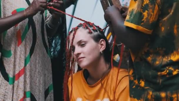 Mujer africana tejiendo trenzas africanas con Kanekalon rojo al aire libre, Zanzíbar África — Vídeo de stock