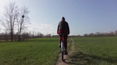 Bisikletli Genç Kadın Güneşli bir ilkbahar gününde Ormanda Bir Yol Üzerinde Geziniyor
