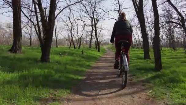 Молодая женщина на велосипеде едет по тропе в лесу в солнечный весенний день — стоковое видео