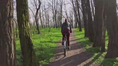 Bisikletli Genç Kadın Güneşli bir ilkbahar gününde Ormanda Bir Yol Üzerinde Geziniyor