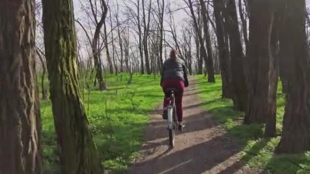Ung kvinna på en cykeltur längs en stig i skogen i en solig Vår i Europa — Stockvideo