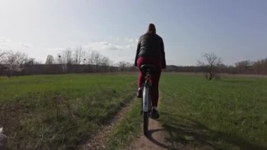 Bisikletli Genç Kadın Güneşli bir ilkbahar gününde Ormanda Bir Yol Üzerinde Geziniyor