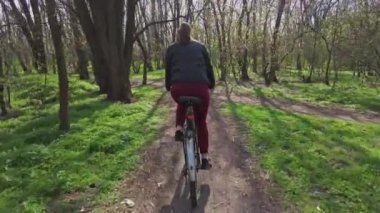 Bisikletli Genç Kadın Güneşli bir ilkbahar gününde Ormanda Bir Yol Üzerinde Geziniyor