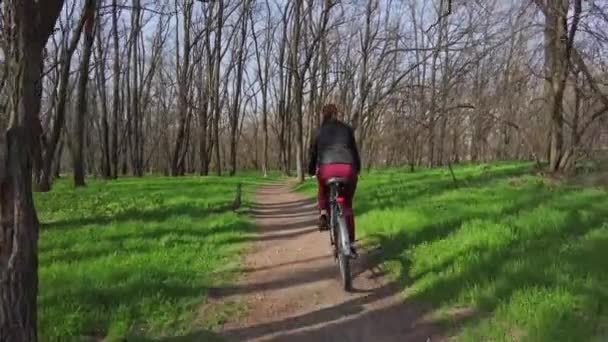 Jovem em um passeio de bicicleta ao longo de um caminho na floresta em um dia ensolarado da primavera — Vídeo de Stock