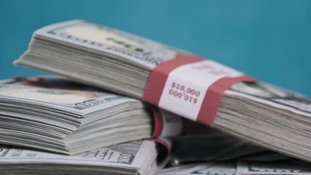 Pacotes de dólares deitados em uma pilha de dinheiro e girar em fundo azul — Vídeo de Stock