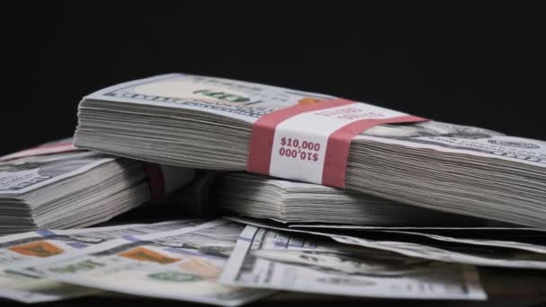 Bundels dollars liggend op een stapel geld en draaiend op zwarte achtergrond — Stockvideo