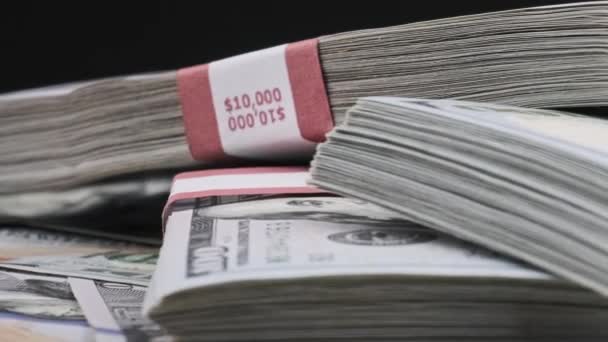 Paquetes de dólares que yacen sobre una pila de dinero y giran sobre el fondo negro — Vídeo de stock
