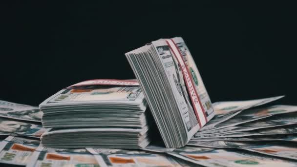 Paquetes de dólares que yacen sobre una pila de dinero y giran sobre el fondo negro — Vídeos de Stock