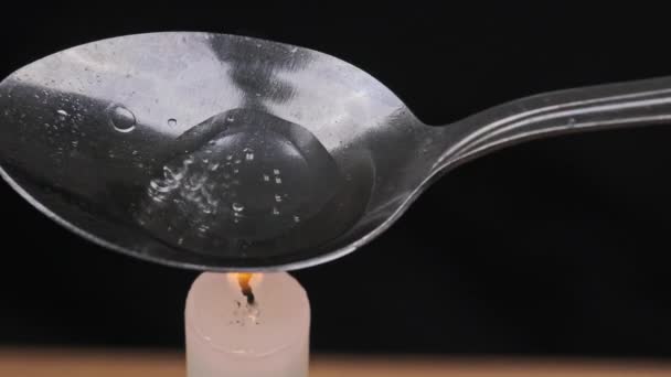 Eine Dosis Heroin in einem Löffel über einer Kerzenflamme zubereiten — Stockvideo