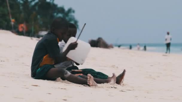 Dva místní afričtí chlapci sedí na pláži a hrají improvizované lahvové bicí, Zanzibar — Stock video