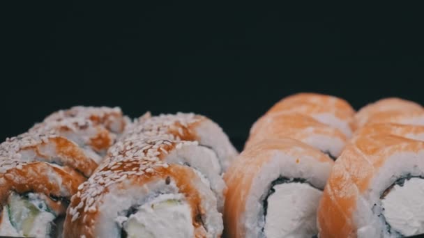 Rolos de sushi girando em caixa de plástico em fundo preto — Vídeo de Stock