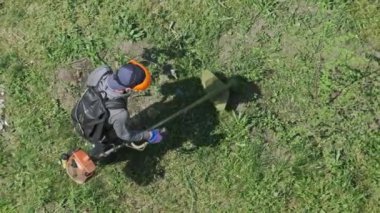 Adam yavaş çekimde çimleri manuel benzin çim biçme makinesiyle biçiyor. Çim biçme makinesiyle çim biçme işlemi. Kamu çalışanının en üst manzarası yeşil çimleri biçiyor. Bahçe bakımı aletleri. Yaz.
