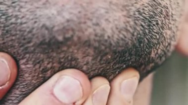 Erkek yumağı yakın plan. Genç adam, sakalına elleriyle dokunuyor. Parmaklarınla çene ovuştur. Makroda siyah tüyleri olan tıraş edilmemiş erkek sakalı. İnsan derisinde saç. Saçları uzamış boyun ve sakal.