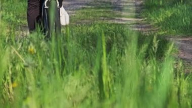 Young woman on a bicycle rides along green forest path in sunny summer day. Slow Motion. Woman on a bike goes on trail way near green grass in countryside. Healthy cycling lifestyle, leisure activity.