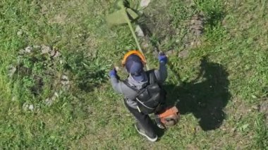 Adam yavaş çekimde çimleri manuel benzin çim biçme makinesiyle biçiyor. Çim biçme makinesiyle çim biçme işlemi. Kamu çalışanının en üst manzarası yeşil çimleri biçiyor. Bahçe bakımı aletleri. Yaz.