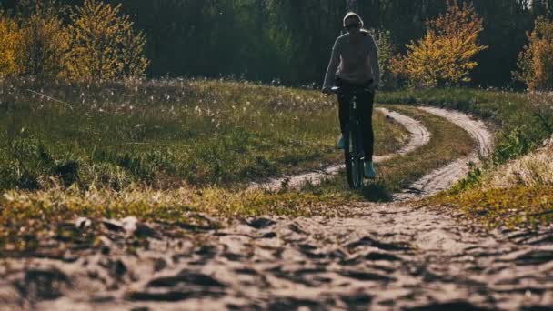 夏の晴れた日に緑の森の道に沿って自転車に乗る若い女性 スローモーション 自転車に乗っている女性は田舎の緑の芝生の近くの道を進みます 健康的なサイクリングライフスタイル レジャー活動 — ストック動画