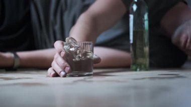 Bir alkolik yere düşer ve yere bir bardak votka dökülmüştür. Aşırı dozda alkol. Alkolizm, sarhoş bir gencin elinin şişenin yanına düşmesi. Yakın plan. Ağır çekim. Alkol bağımlılığı