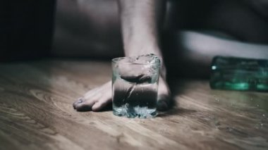 Bir alkolik yere düşer ve yere bir bardak votka dökülmüştür. Aşırı dozda alkol. Alkolizm, sarhoş bir gencin elinin şişenin yanına düşmesi. Yakın plan. Ağır çekim. Alkol bağımlılığı