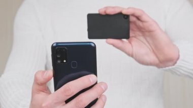 Modern bir şifreleme cüzdanı ve akıllı telefonuyla QR kodu taranıyor. Beyaz arka plandaki genç adam cihazların kamerasını kullanarak işlem yapıyor. Bitcoin göndermek, işlem, dijital nakit konsepti. 4K.