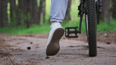 Bisikletli genç bir kadın yaz günü orman yolunda ağır çekimde bisiklet sürüyor. Kırsal bir parkta yeşil ağaçların arasında bisiklet süren bir kadın. Spor yaşam tarzı, boş zaman aktivitesi, tatil