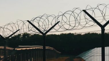 Gün batımında güneş enerjisi santralinin etrafında dikenli teller var. Çit örgüsü. Güneş enerjisi elementlerinin bulunduğu bölgeyi çitliyor. Dikenli tellerin arkasındaki güneş panelleri alanı.
