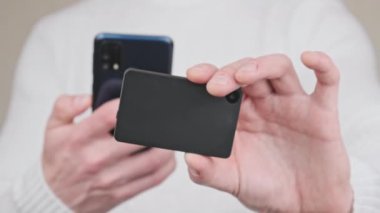 Modern bir şifreleme cüzdanı ve akıllı telefonuyla QR kodu taranıyor. Beyaz arka plandaki genç adam cihazların kamerasını kullanarak işlem yapıyor. Bitcoin göndermek, işlem, dijital nakit konsepti. 4K.
