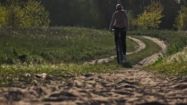 夏の晴れた日に緑の森の道に沿って自転車に乗る若い女性 スローモーション 自転車に乗っている女性は田舎の緑の芝生の近くの道を進みます 健康的なサイクリングライフスタイル レジャー活動 — ストック動画