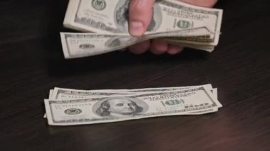 Siyah ahşap bir masada eski 100 dolarlık banknotları saymak. Erkek eller kağıt para sayıyor, ev parası. 100 dolarlık banknotlar sayan bir elin yakın çekimi. İş, finans, ekonomi kavramı.