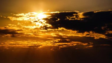 Güneş ışınlarının turuncu katmanlı bulutlar arasından gökyüzüne vurduğu dramatik bir gün batımı, Timelapse. Büyük parlak sarı güneş ufuktan aşağı doğru hareket ediyor. Zaman aşımı. Destansı bulut uzayı. İnanılmaz canlı gün batımı