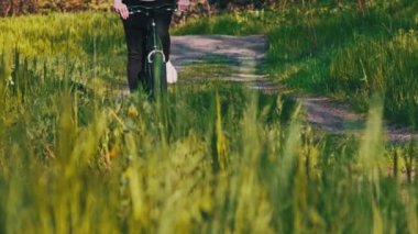 Güneşli bir yaz gününde yeşil bir ormanda bisiklet süren bir kadın. Ağır çekim. Bisikletli bir kadın kırsal alandaki çayırların çok yakınında geziyor. Boş zaman aktivitesi, sağlıklı bisiklet yaşam tarzı
