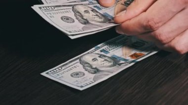 Siyah ahşap bir masadaki yeni yüz dolarlık banknotları sayıyorum. Erkek eller kağıt para sayıyor, ev parası. 100 dolarlık banknotlar sayan bir elin yakın çekimi. İş, finans, ekonomi kavramı.