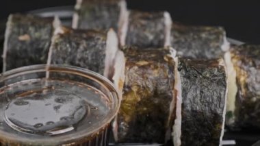 Japanese sushi rolls in plastic box is rotating, close-up. Takeaway fresh sushi with ginger, wasabi and soy sauce. Many sushi with Philadelphia cheese, nori, crab sticks, salmon fillets and cucumber.