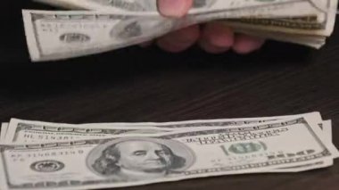 Siyah ahşap bir masada eski 100 dolarlık banknotları saymak. Erkek eller kağıt para sayıyor, ev parası. 100 dolarlık banknotlar sayan bir elin yakın çekimi. İş, finans, ekonomi kavramı.