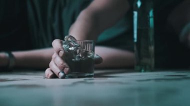 Sarhoş bir adam bir bardak votka ve aşırı dozda alkolle yere düşüyor. Ağır çekim. Alkol bağımlılığı. Sarhoş bir gencin eli şişenin yanına düştü. Yakın plan. Alkolizm, Bağımlılık