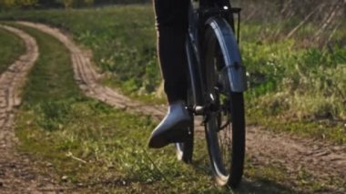 Woman on bicycle rides along forest path in a green forest on a sunny summer day. Slow Motion. Woman on bike goes on trail way near meadows in countryside. Leisure activity, healthy cycling lifestyle
